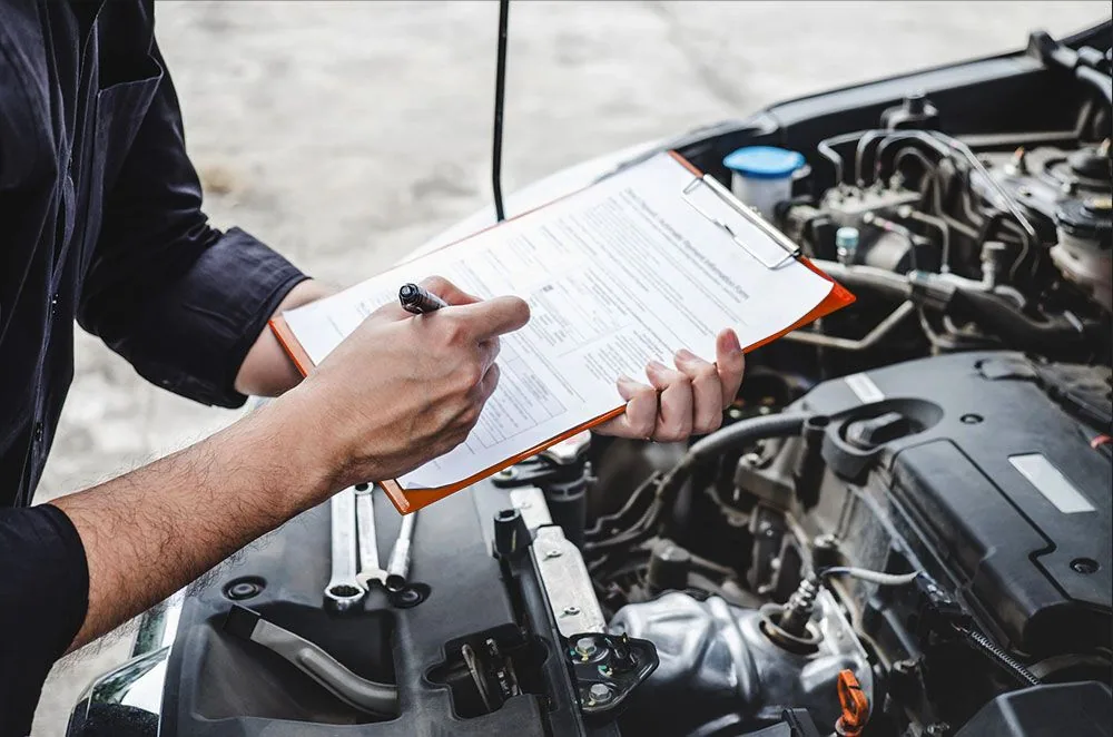 A mechanic is writing on a clipboard while working on a car.