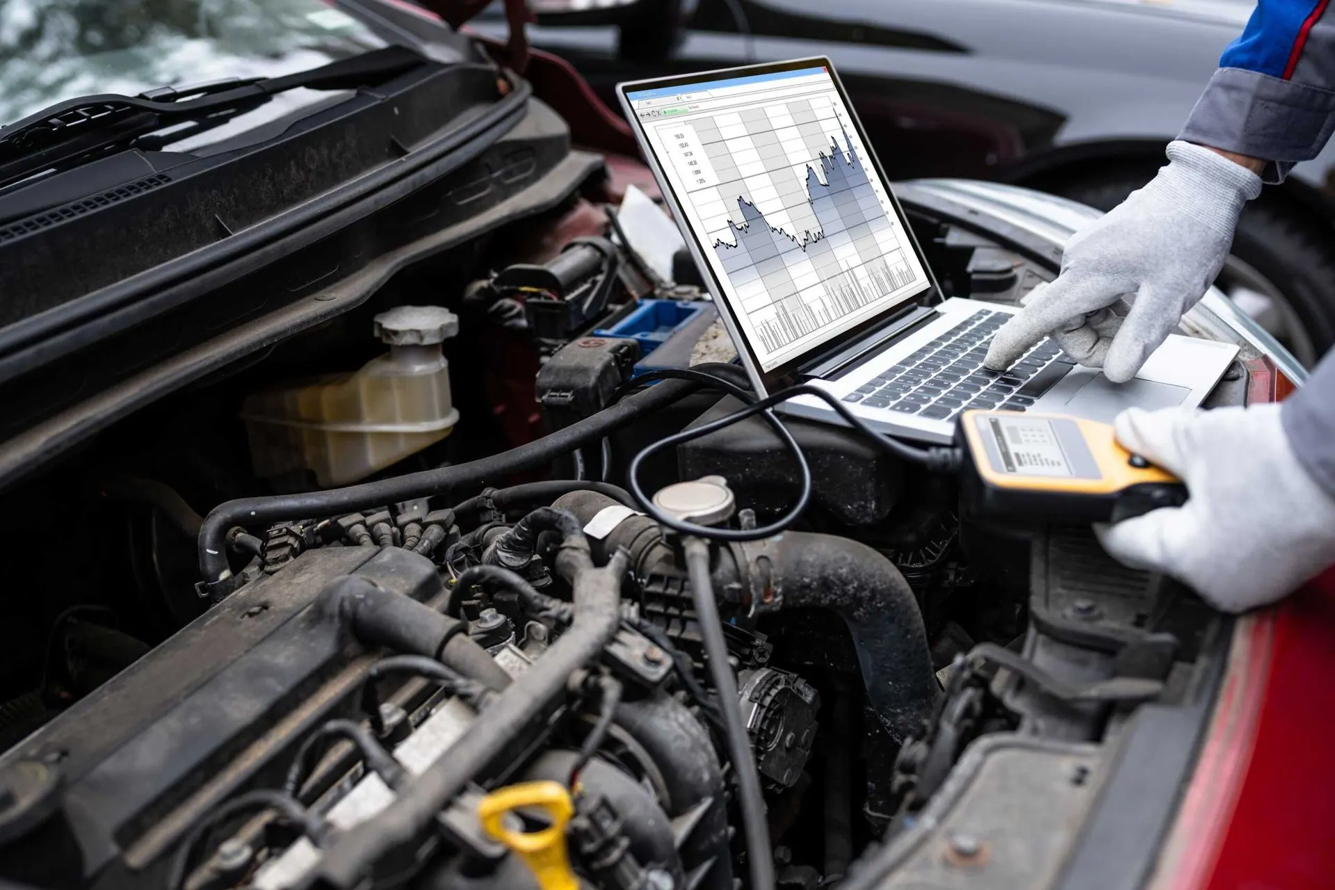 A mechanic is using a laptop computer to check the engine of a car.